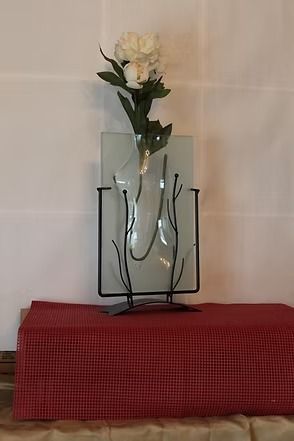 White flower in glass vase on metal stand atop a red checkered tablecloth.