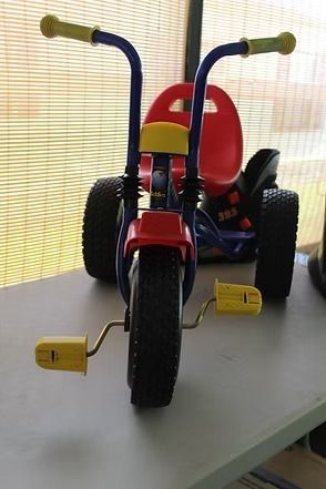 Red child’s tricycle with yellow pedals and blue handlebars on a tabletop.