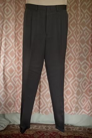 Black pleated trousers hanging against a patterned pink curtain