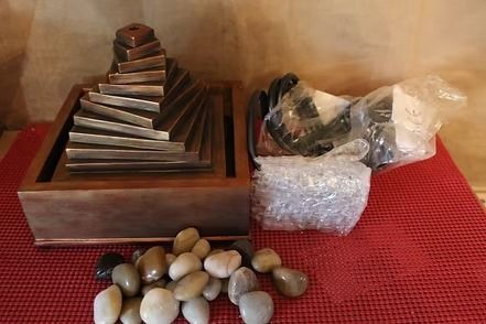 Metal staircase model on wooden base beside bubble wrap and small stones on a red mat
