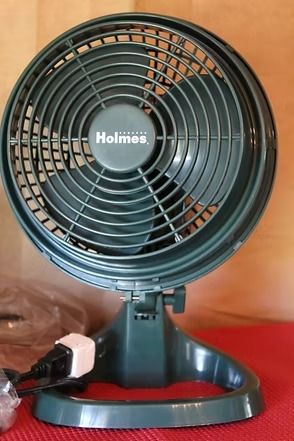 Black Holmes desk fan on a red surface against a tan background