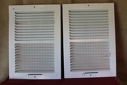 Two white louvered vent covers with adjustable slats, side by side against a wall