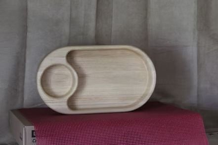 Wooden serving tray with a round bowl inset, resting on a pink textured surface against gray curtains