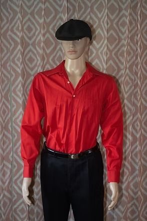 Mannequin wearing a red shirt, black pants, and black cap against a patterned curtain background