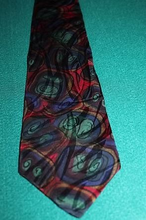 Colorful patterned necktie with red, green, and blue swirls on a teal surface