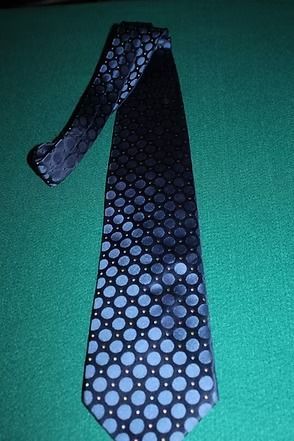 Black necktie with blue polka dots on a green surface
