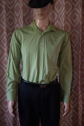 Mannequin wearing a light green button-up shirt and dark pants in side profile against a patterned curtain.