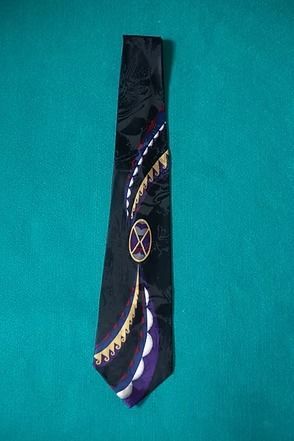 Black patterned necktie with purple and gold accents hanging on a teal background