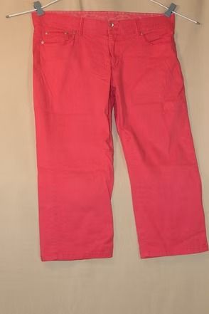 Red pants hanging on a hanger against a beige background.