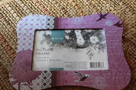 Purple floral picture frame on a woven mat, wrapped with a label and barcode.