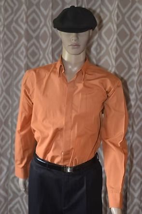 Mannequin wearing an orange shirt, dark pants, and black cap against a patterned backdrop.