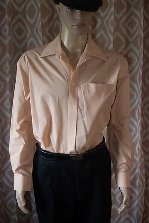 Mannequin wearing a peach button-up shirt, black pants, and a black hat against a patterned backdrop