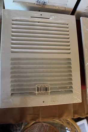 White vent cover with slats and barcode label, lying on a wooden floor.
