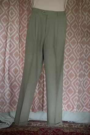 Light olive green trousers hanging in front of a patterned curtain and rug.