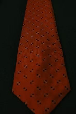 Orange necktie with a small black diamond pattern on a dark background