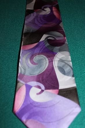 Purple and gray patterned necktie laid on a teal surface.