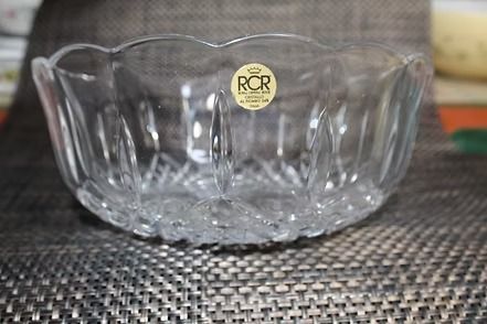 Clear glass bowl with scalloped edges and a gold sticker, on a textured placemat.