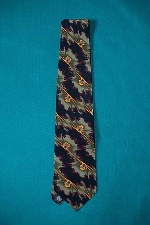 Narrow patterned necktie with blue, yellow, and burgundy zigzag design on a teal background