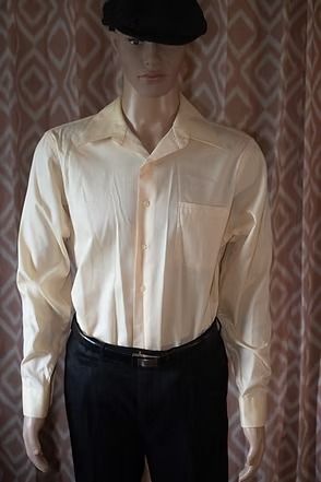 Mannequin wearing a cream button-up shirt, black pants, and a black hat against a patterned curtain backdrop