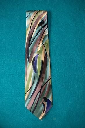 Colorful patterned necktie hanging against a teal wall