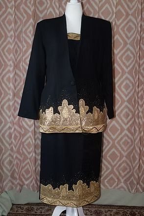 Black jacket and skirt with gold trim displayed on a mannequin against patterned curtains