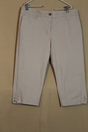 Light gray pants hanging on a hanger against a beige background