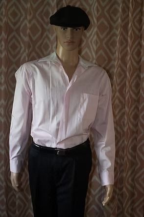 Mannequin wearing a pale pink dress shirt, dark trousers, and a black cap against patterned wallpaper