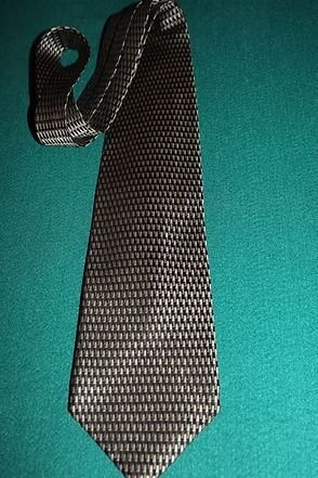 Black patterned necktie with a textured fabric, laid on a teal background
