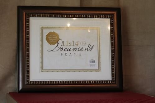 Framed document displayed on a shelf against a beige wall