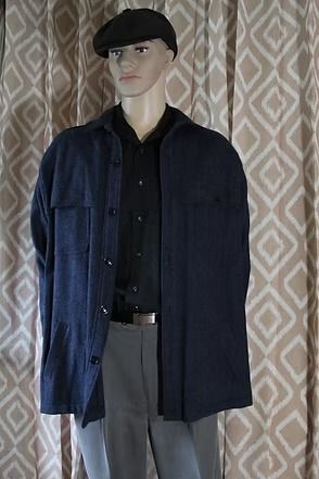 Mannequin wearing a dark jacket, black shirt, gray trousers, and a black beret against a patterned curtain.