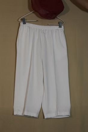 White pants hanging on a hanger against a plain wall