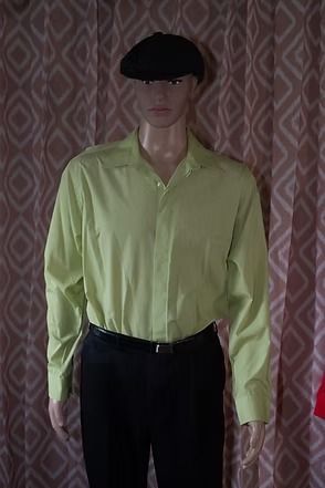 Mannequin wearing a lime green shirt, black pants, and black hat against patterned curtains
