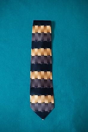 Patterned necktie with dark navy, gold, and beige geometric stripes on a teal background