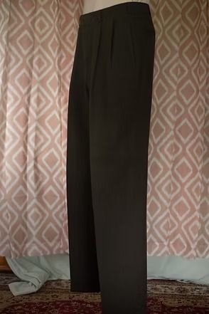 Black slim-fit pants hanging against a patterned curtain backdrop.