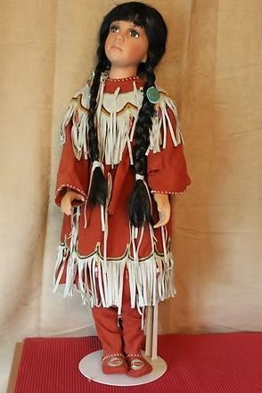 Native doll in red and white traditional dress with long black braids on a stand