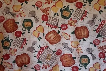 Patterned tablecloth with pumpkins, apples, bread, and fruit on a light background