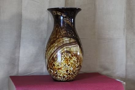 Decorative glass vase with brown and gold swirls on a red textured cloth