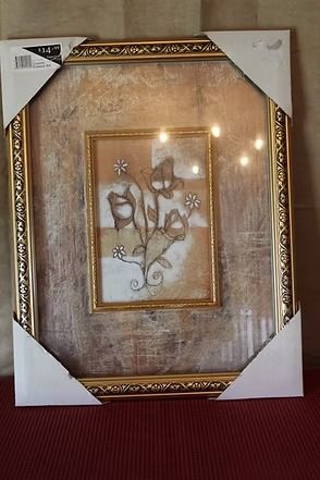 Framed floral artwork with gold trim, leaning against a wooden wall on a red surface