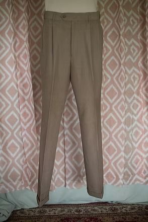 Beige trousers hanging against a patterned curtain backdrop.