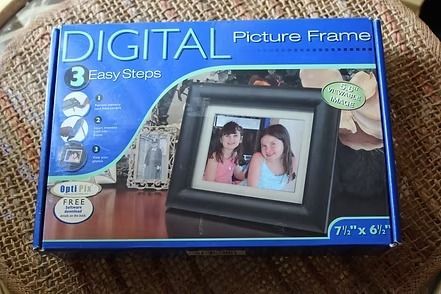 Blue digital picture frame retail box on a woven surface, showing a black frame with two people inside.