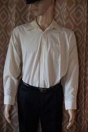Mannequin wearing a cream button-up shirt, black pants, and a black hat against patterned wallpaper.