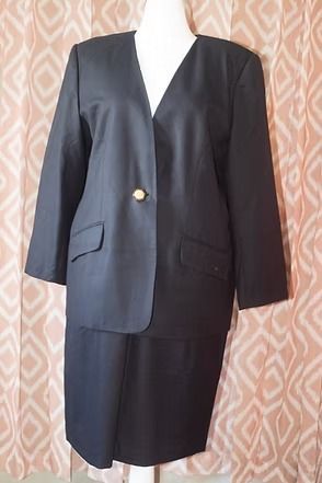 Black blazer with gold button over a black skirt on a hanger against a patterned background