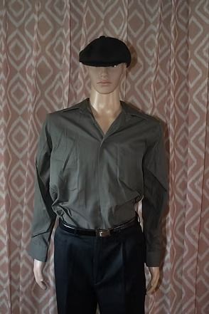 Mannequin wearing a dark cap, gray shirt, and black pants against a patterned curtain backdrop