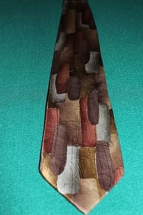 Patterned necktie with brown, tan, white, and red geometric shapes on a teal background