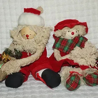 Two plush teddy bears in red and white Christmas outfits sitting on a white quilted blanket.