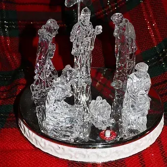 Clear ice sculpture on a red plaid cloth with three standing figures around a central scene
