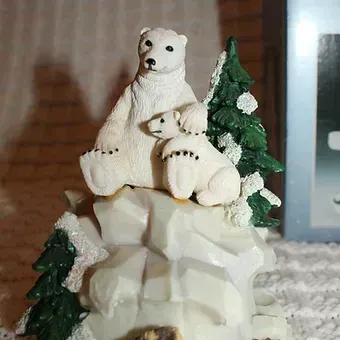 White polar bear figurine sitting on a snowy rock with small pine trees, festive winter decor