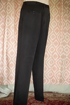 Black dress pants hanging upright in front of patterned curtains.