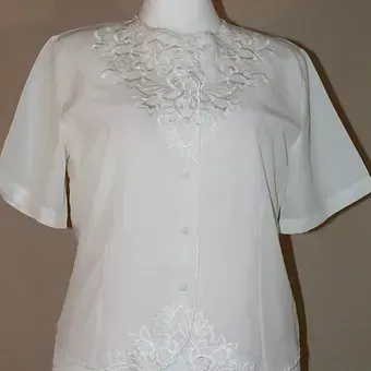 White short-sleeve blouse with floral embroidery on the chest and hem, shown on a mannequin