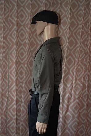 Mannequin wearing a dark cap, gray shirt, and black pants against a patterned curtain backdrop